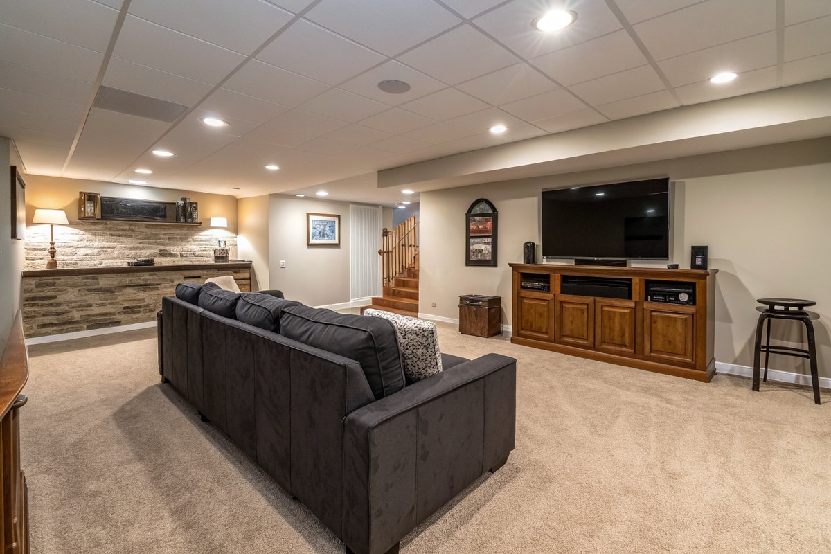 A dry finished basement media room with a gray sofa, a TV console and beige carpet